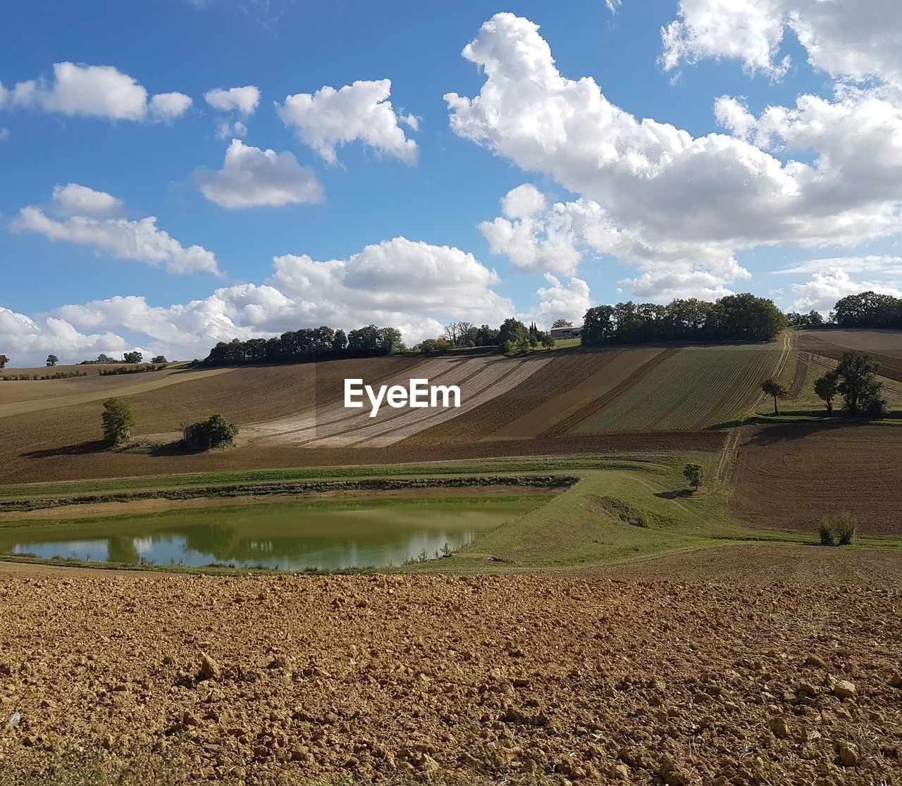 Pond by agricultural field against sky