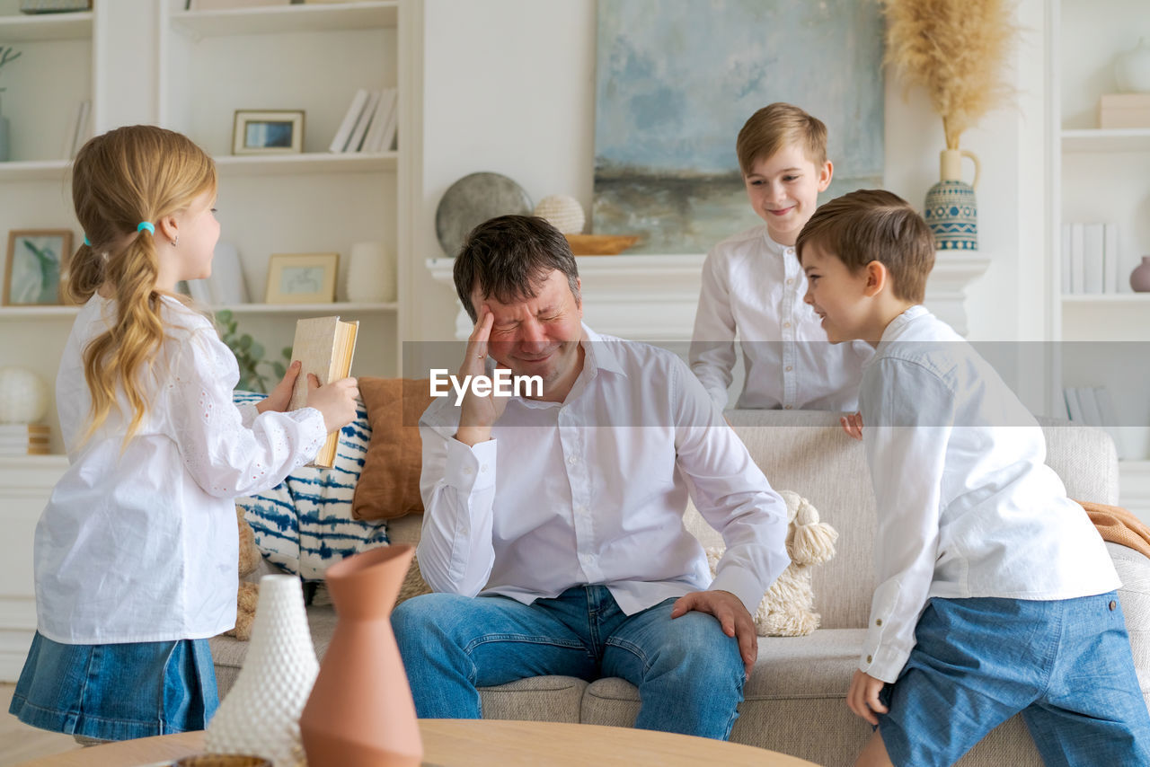 An annoyed father sitting on sofa at home in living room distracted from noise