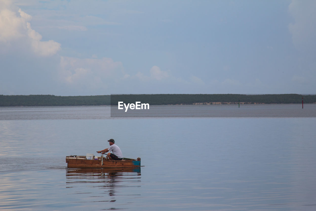 Man sitting on boat over lake against sky