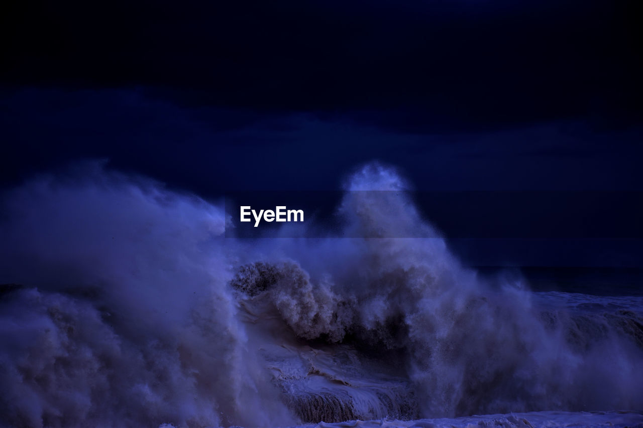 Wave splashing in sea against sky at night