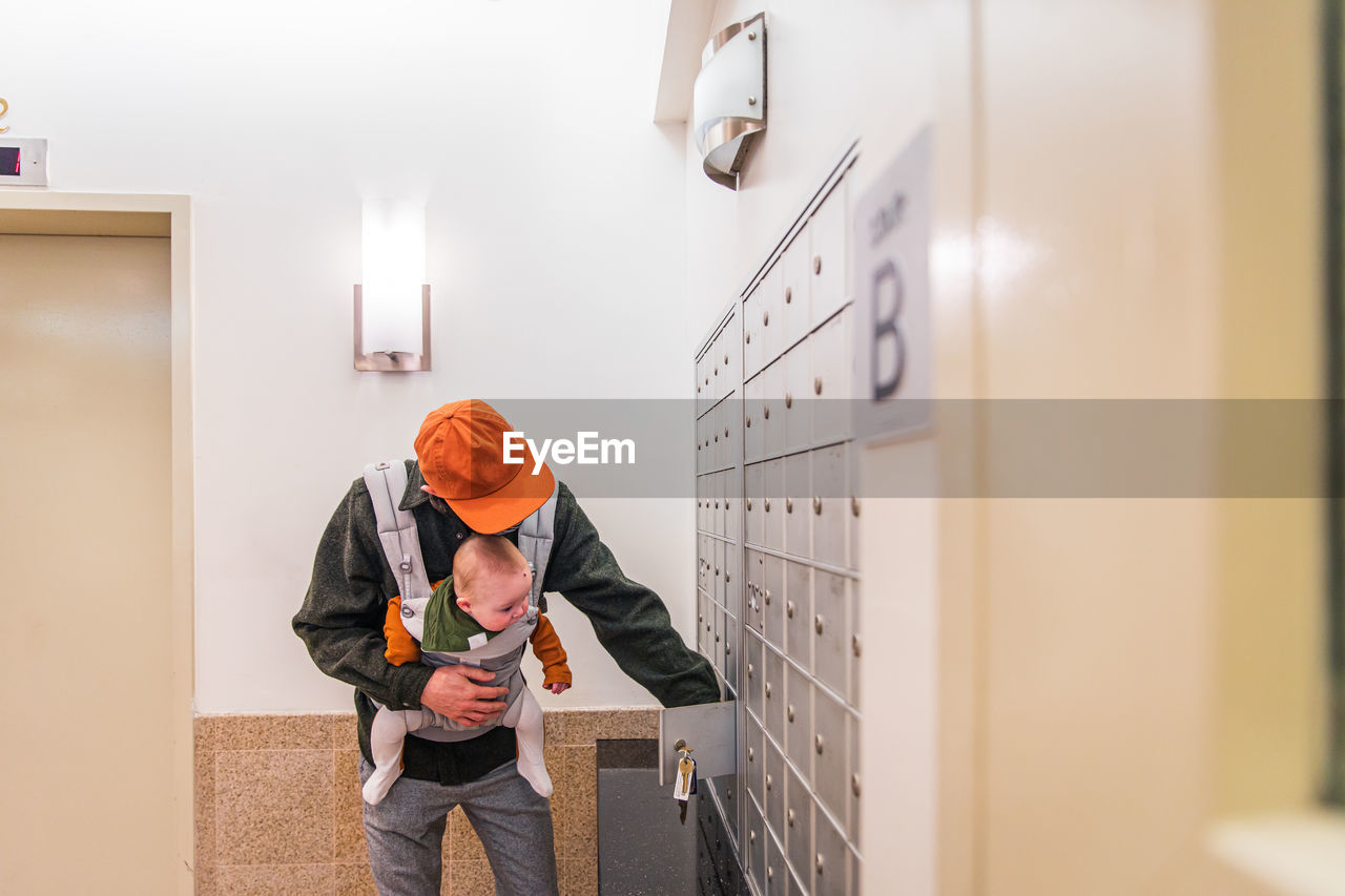 Father carrying daughter in carrier opening locker in room while during pandemic