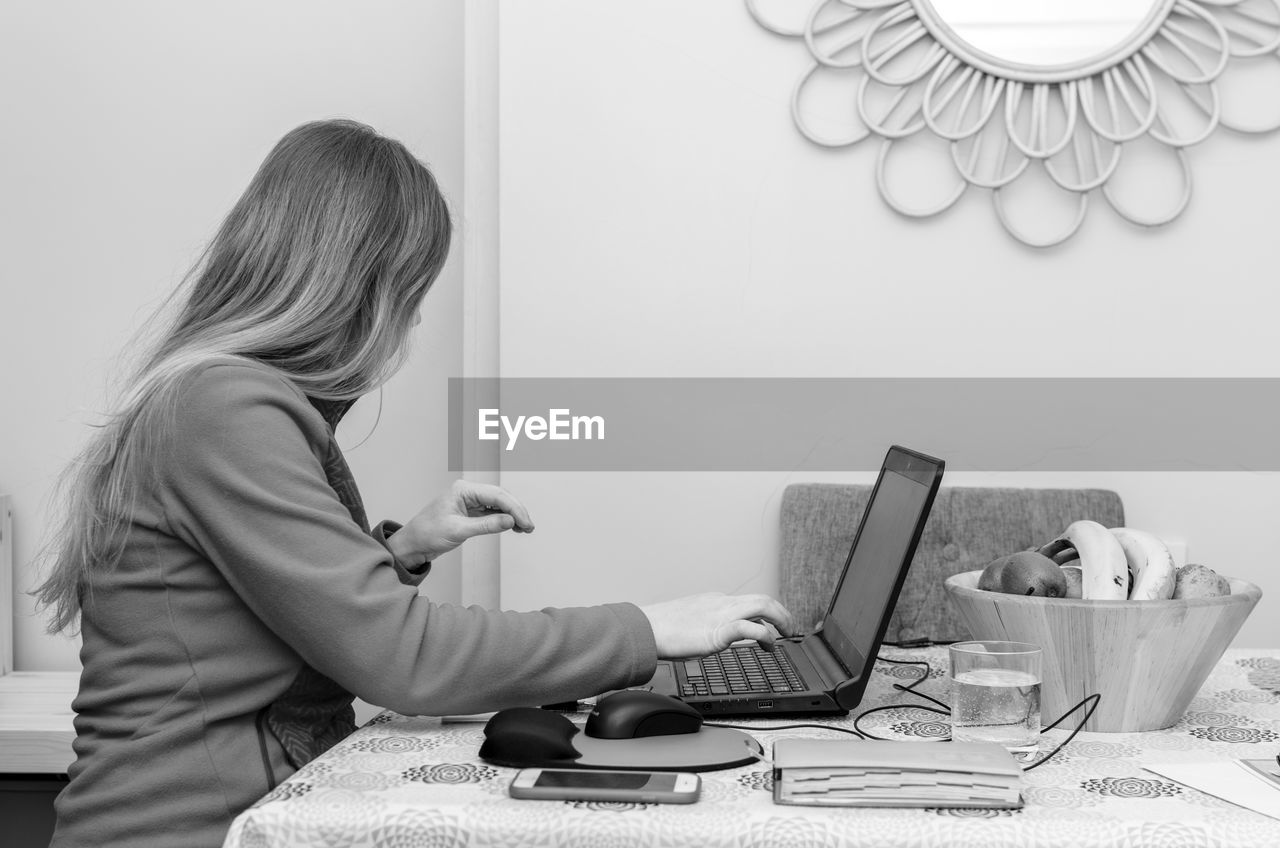 SIDE VIEW OF WOMAN USING SMART PHONE AT HOME