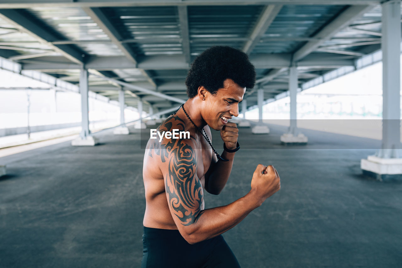 Shirtless male boxer practicing below bridge