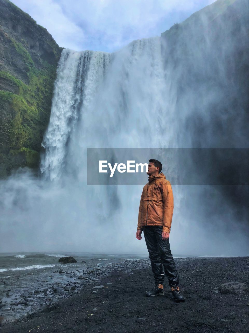 Full length of man standing by waterfall on mountains