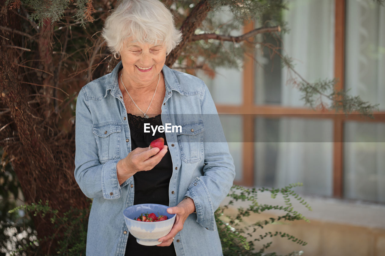 Elderly woman holding a bowl of ripe strawberries