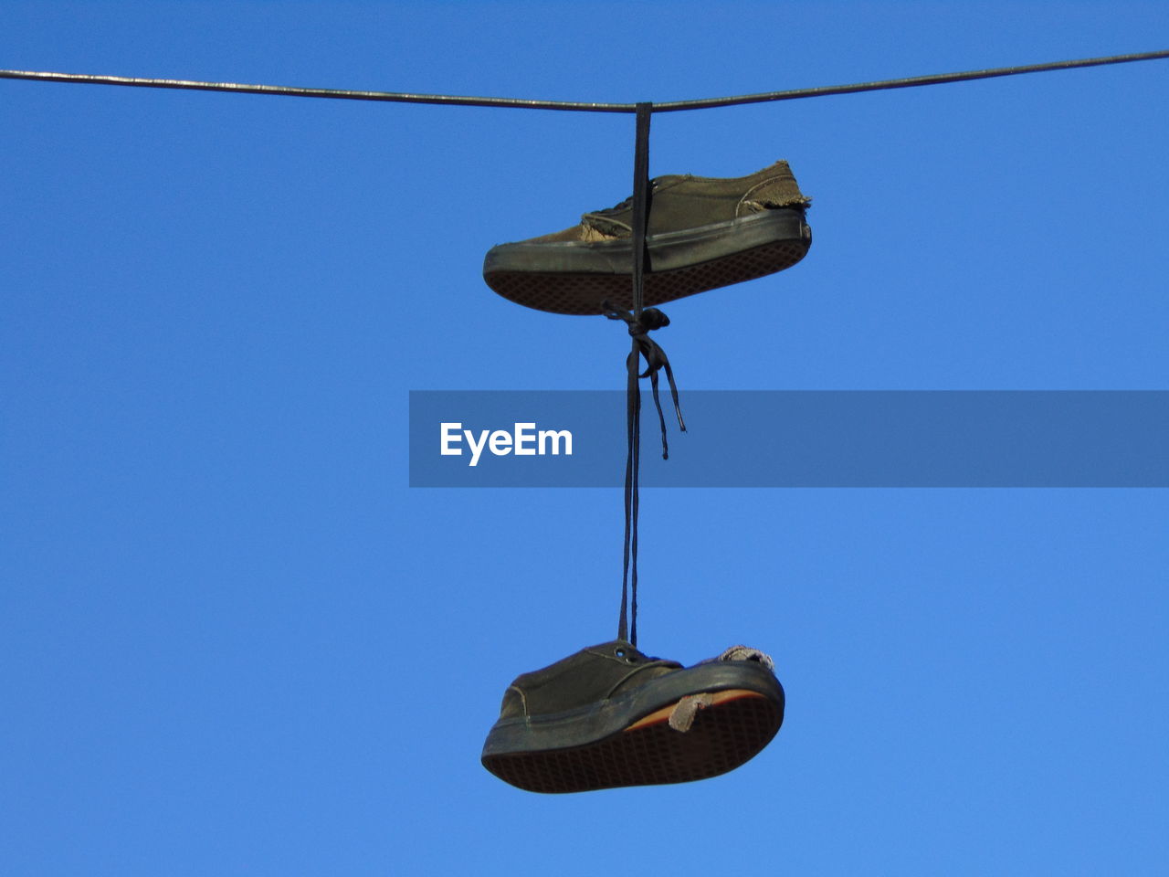 Low angle view of shoes hanging on cable against clear blue sky