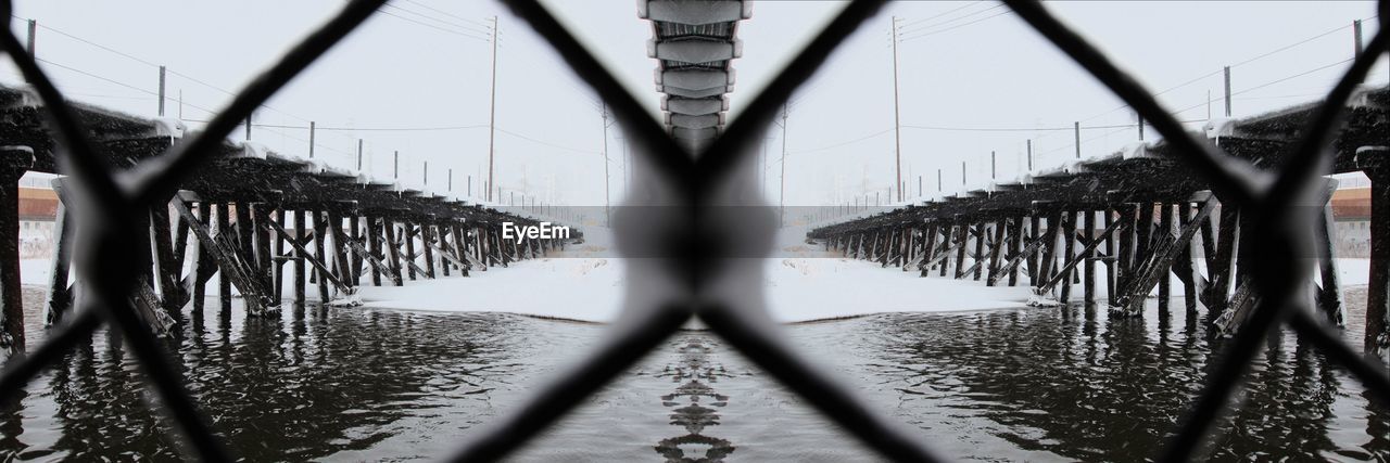 Pier in river seen through chainlink fence during winter