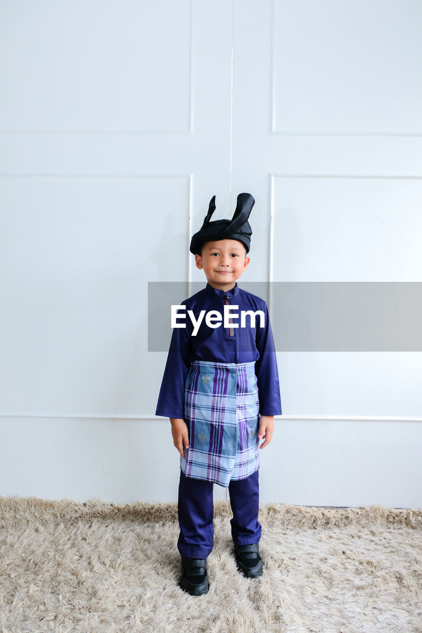 Portrait of cute boy wearing traditional clothing standing against wall