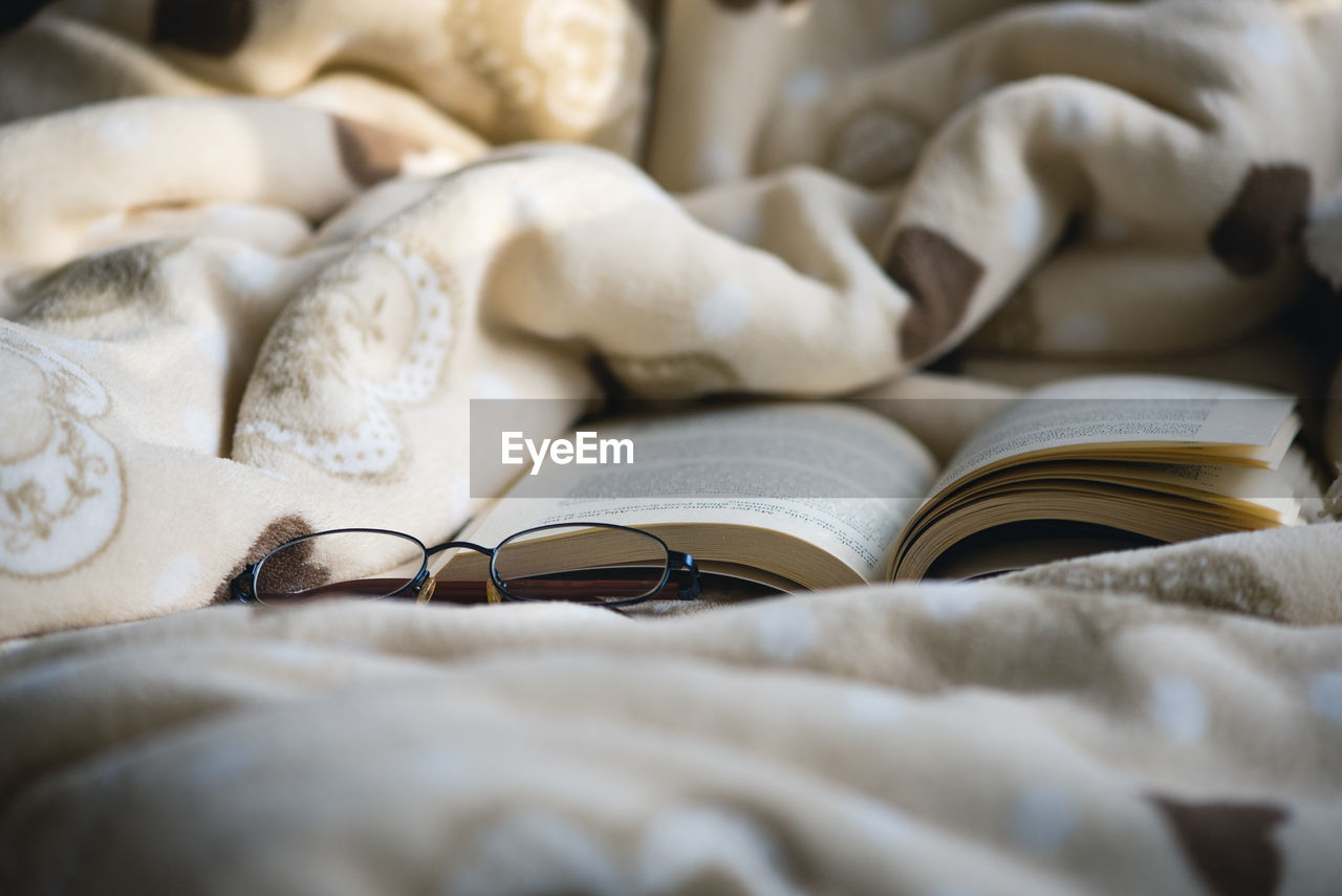 Close-up of open book and eyeglasses on bed