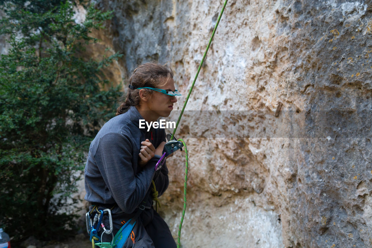 Side view of hiker holding rope while standing by rock