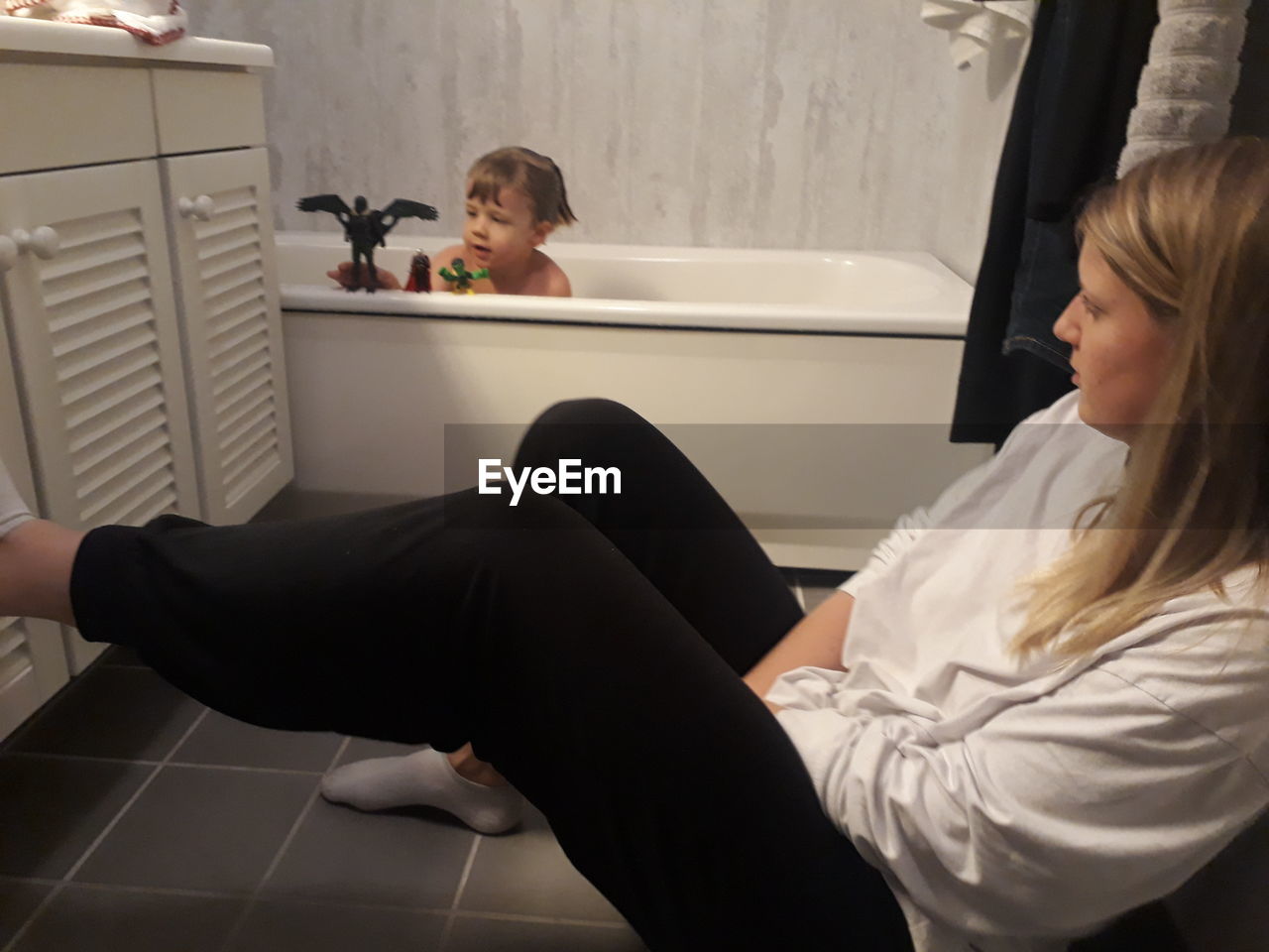 Woman looking at boy playing with toys in bathtub at home