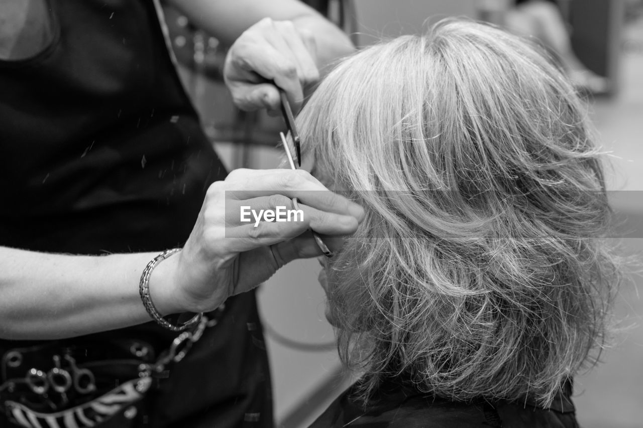 Midsection of hairdresser cutting woman hair in salon