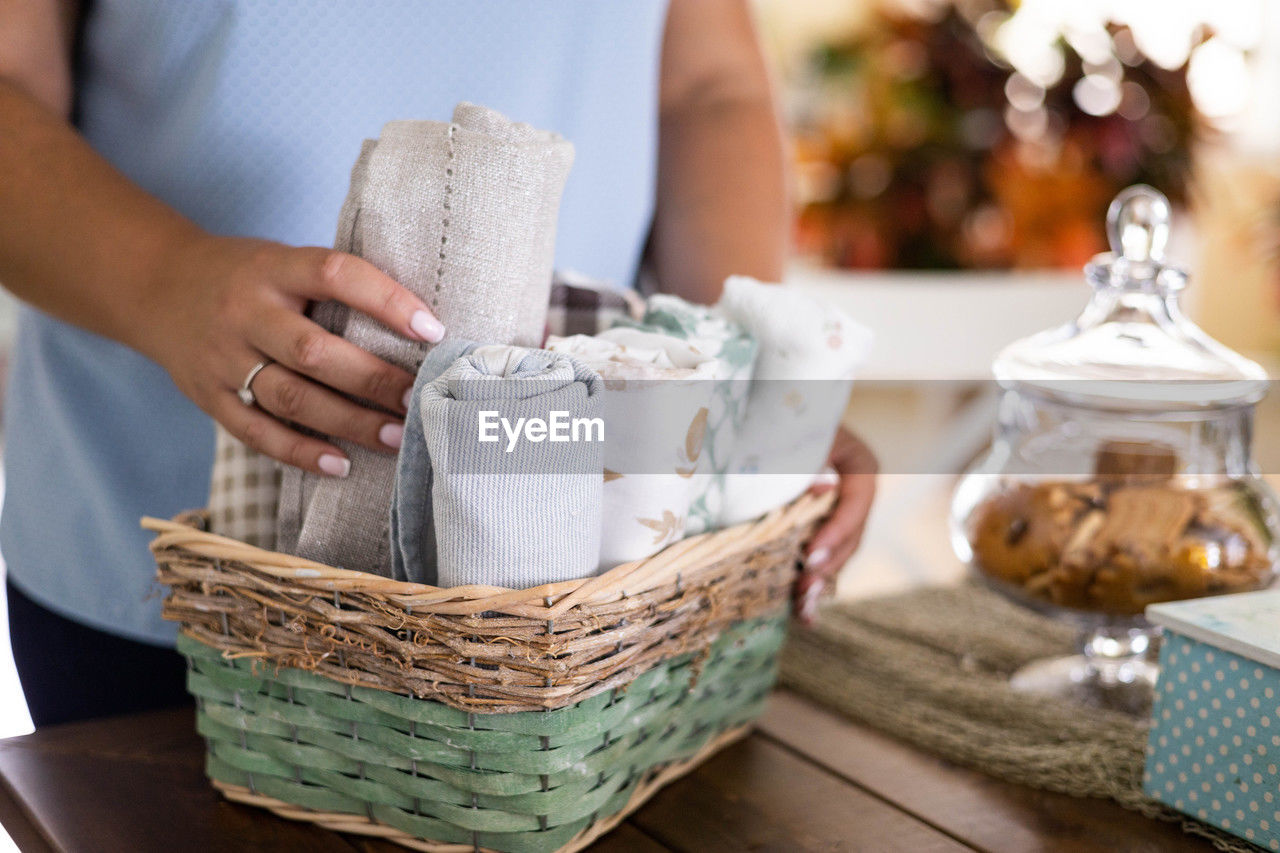 midsection of woman holding wicker basket on table