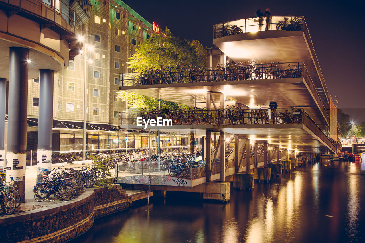 Low angle view of illuminated buildings by canal at night