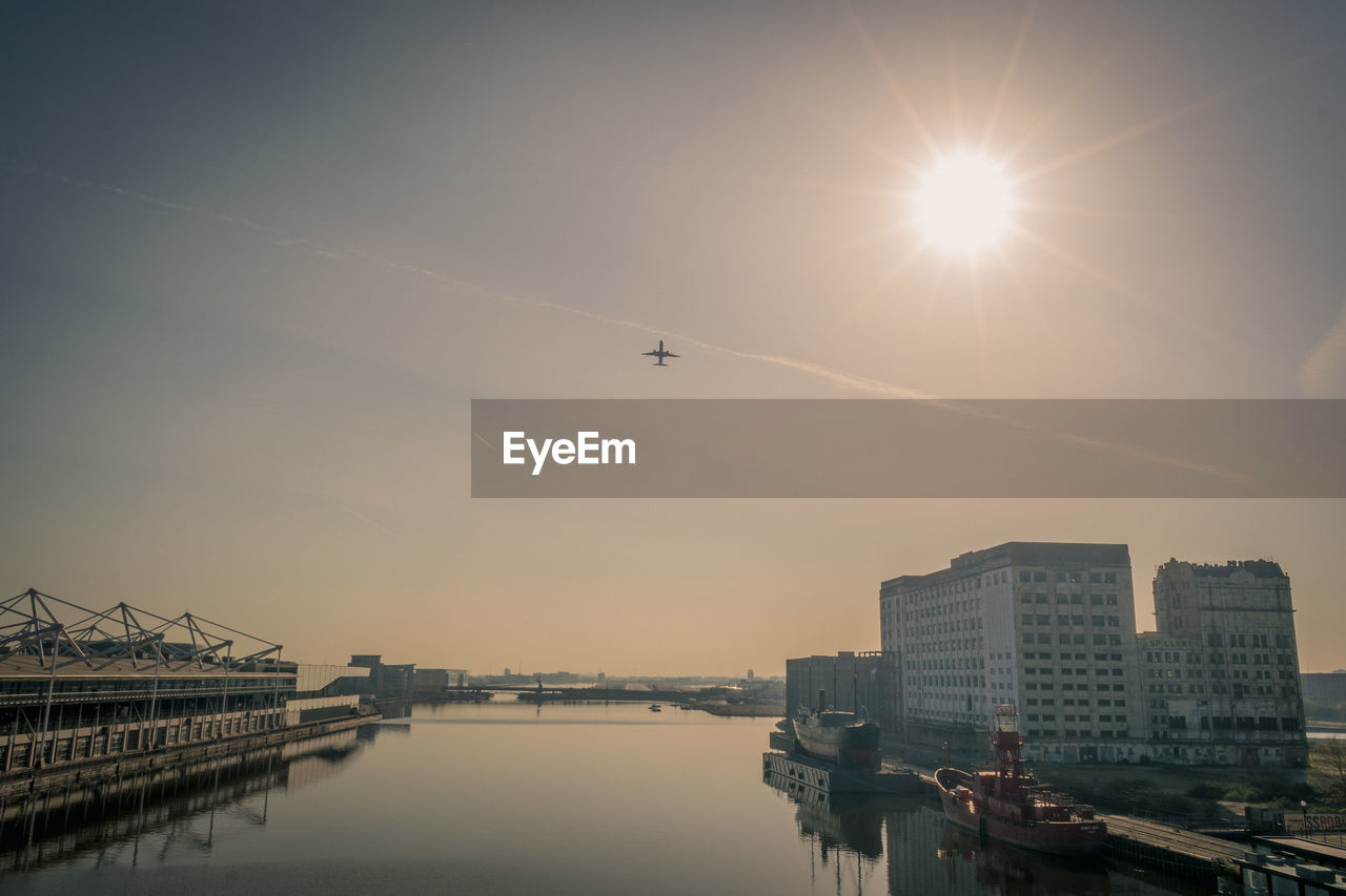 Airplane flying over city against sky during sunset