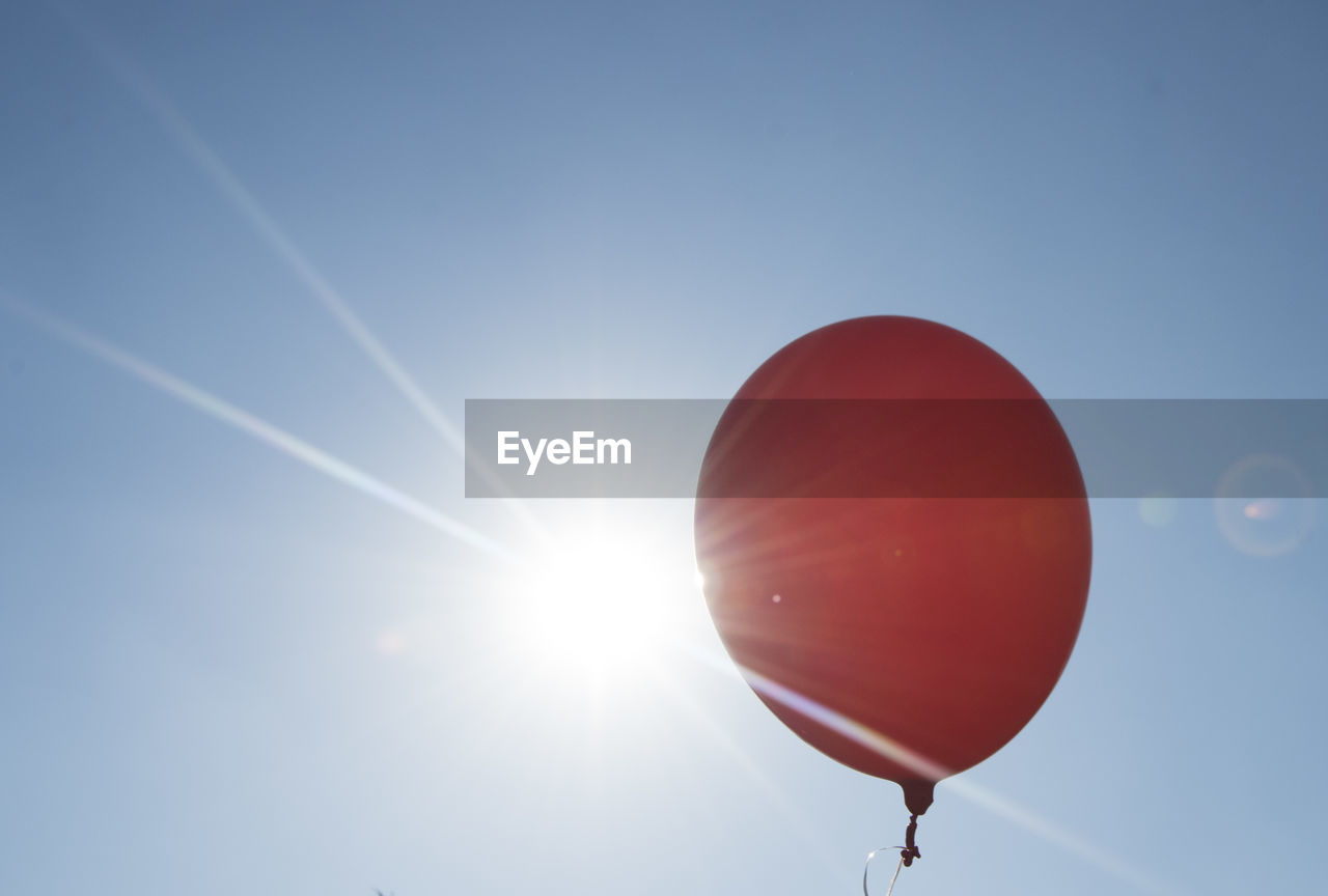 Red balloon and blue sky background with sun, symbol for joy and happiness