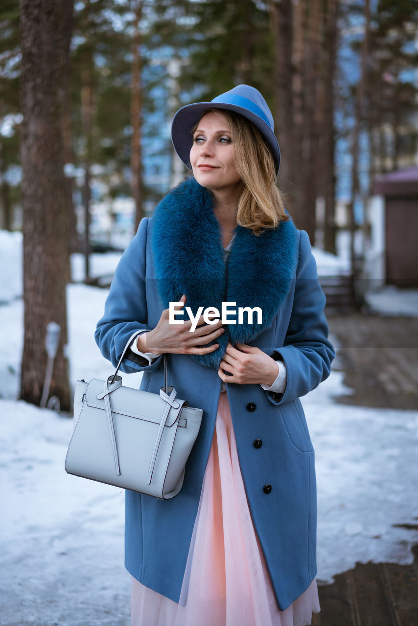 Beautiful woman in blue coat and hat posing outdoors in the snow