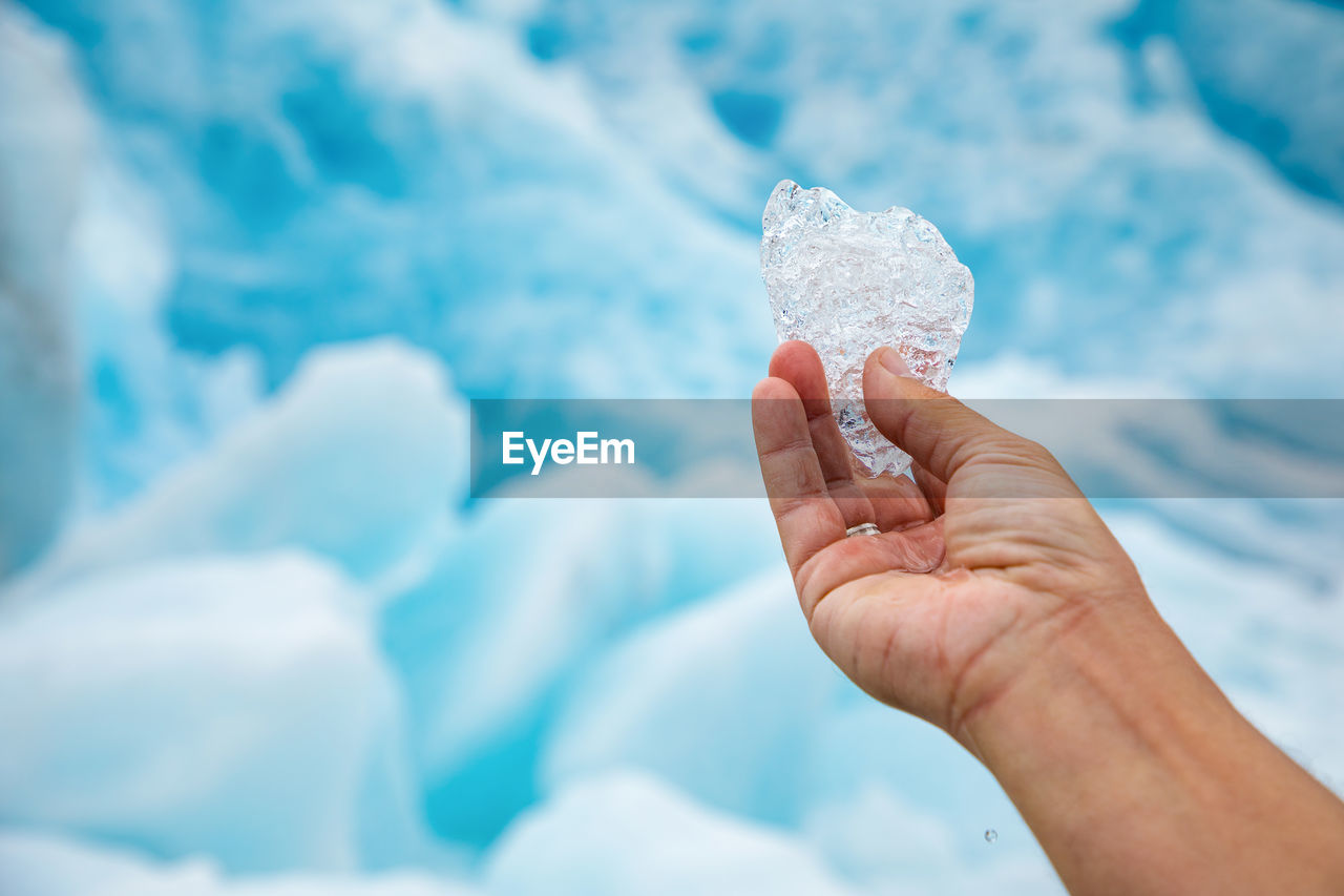 Cropped image of person hand holding ice against icebergs