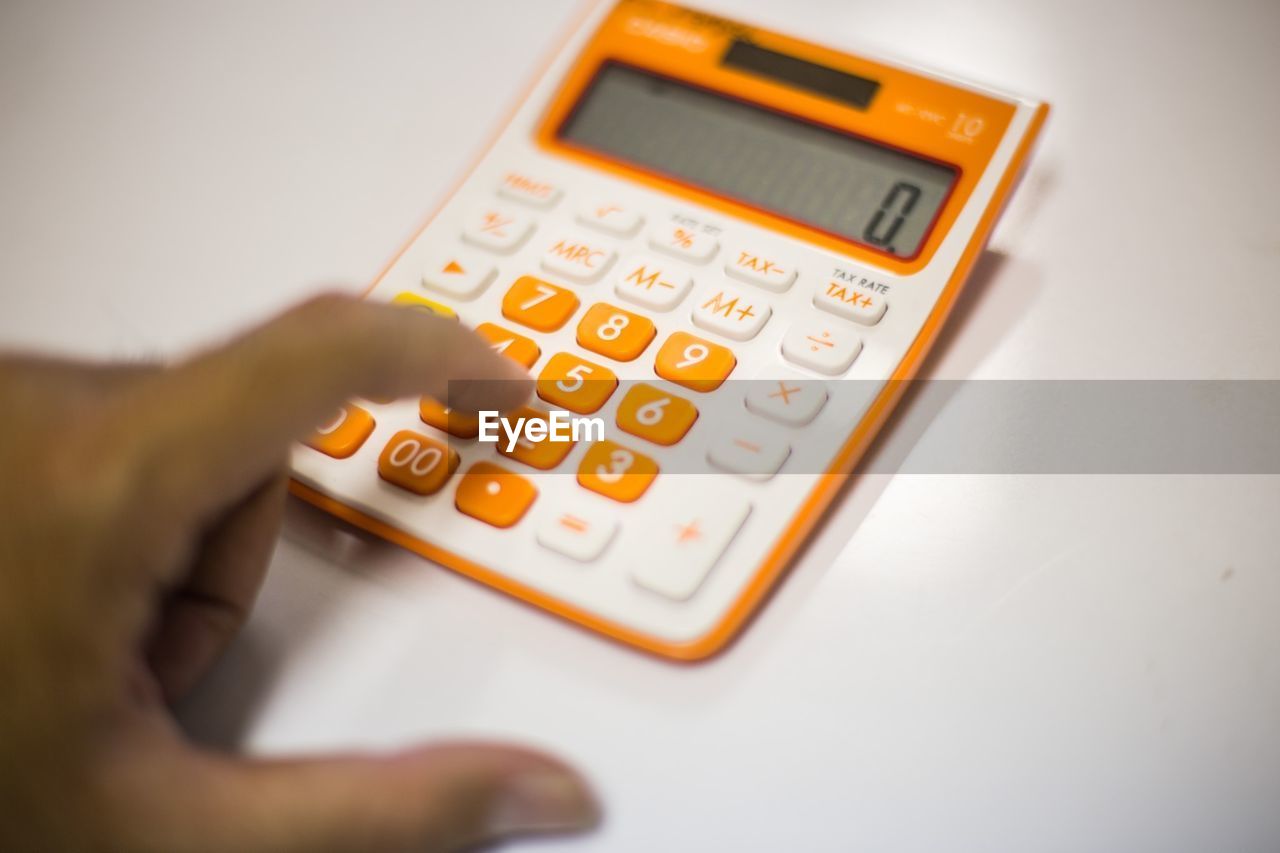 Cropped hand of person using calculator on white table