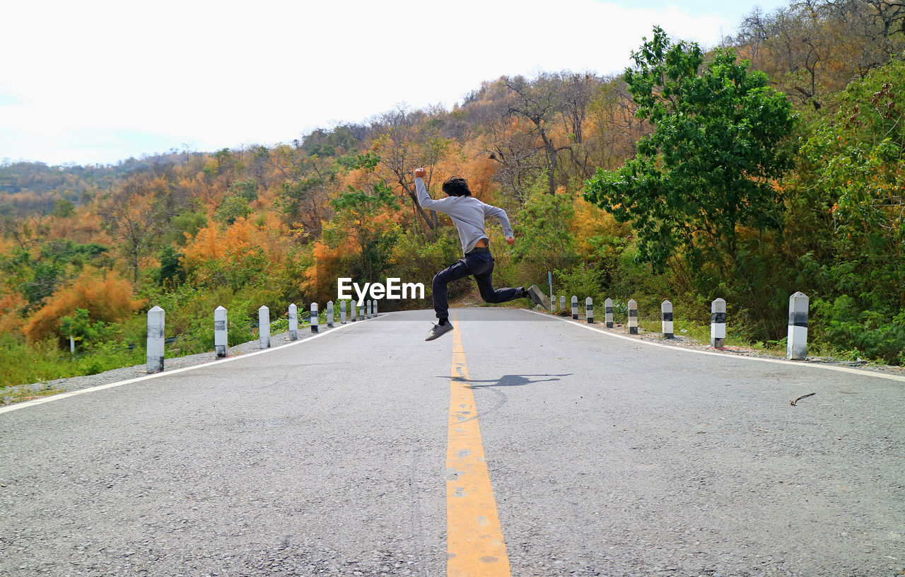 Full length of man jumping on road amidst trees