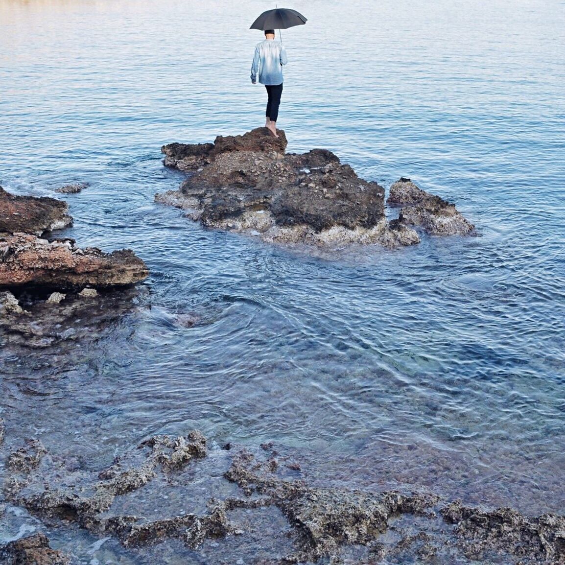 REAR VIEW OF WOMAN STANDING ON ROCK AT SEA