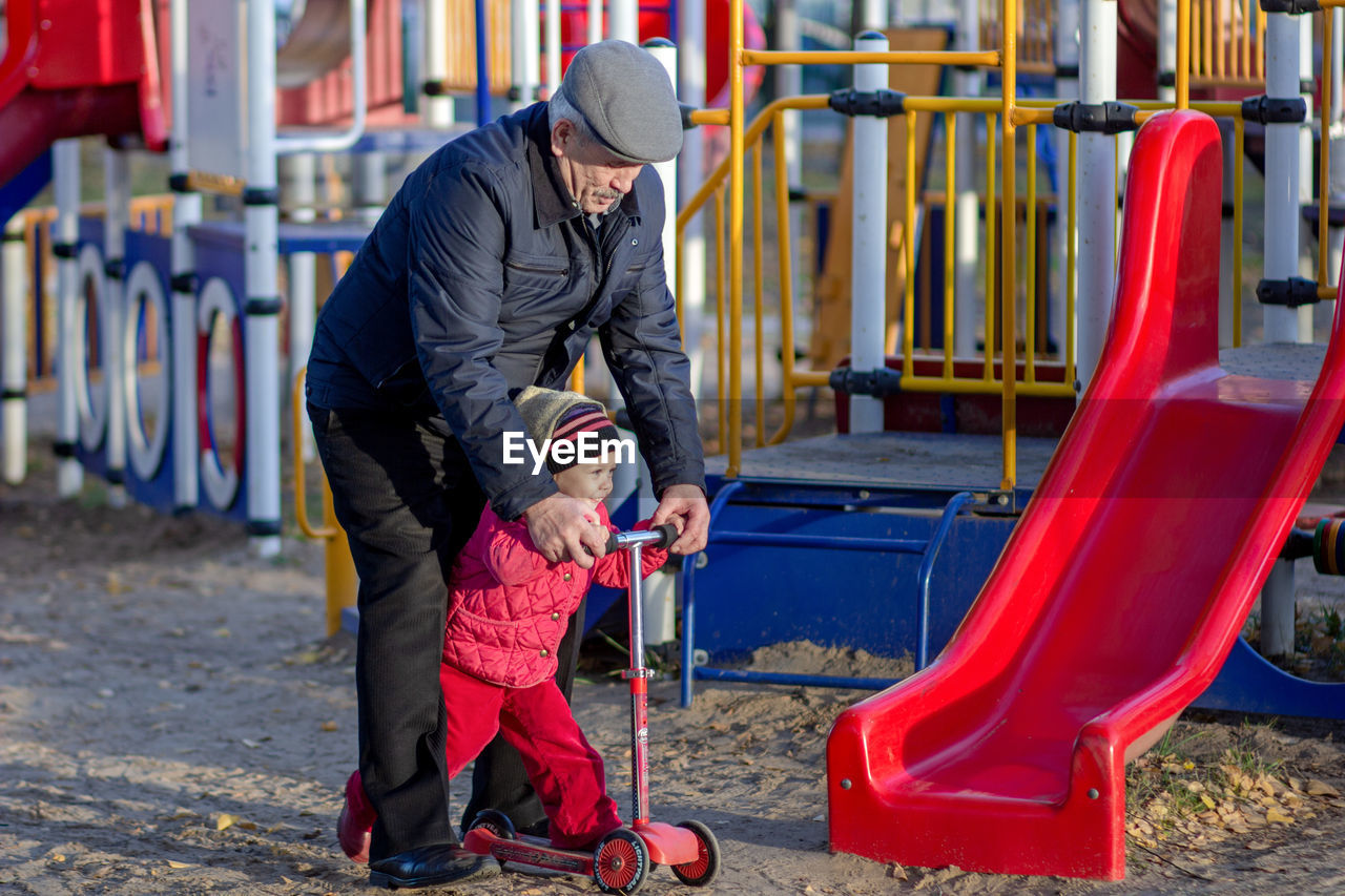 Grandfather helping granddaughter to ride on scooter