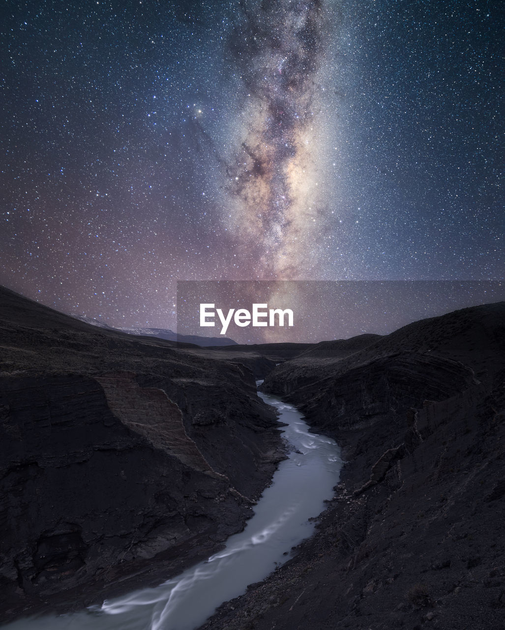 Scenic view of stream amidst mountains against star field at night