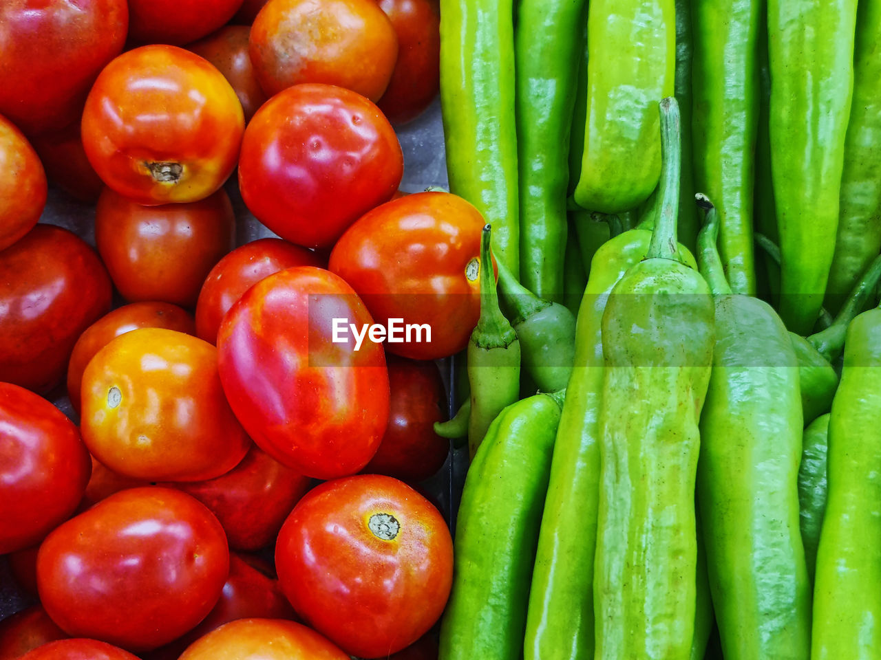 Close-up pile of fresh red tomatoes and green chili peppers for sale