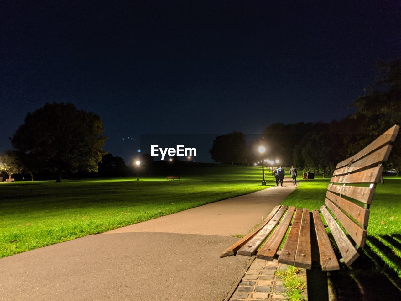 Empty park bench by street against sky at night