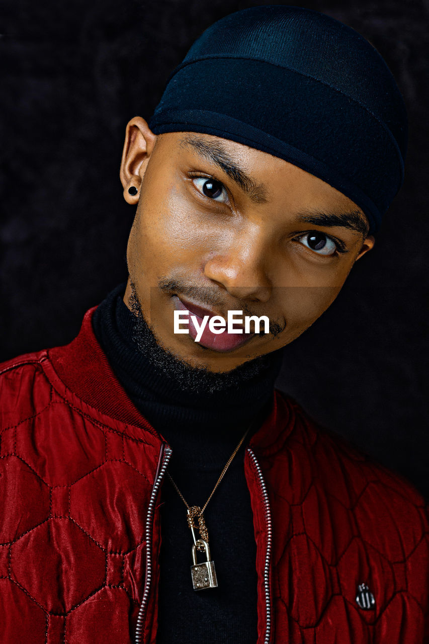 Portrait of young man wearing hat against black background