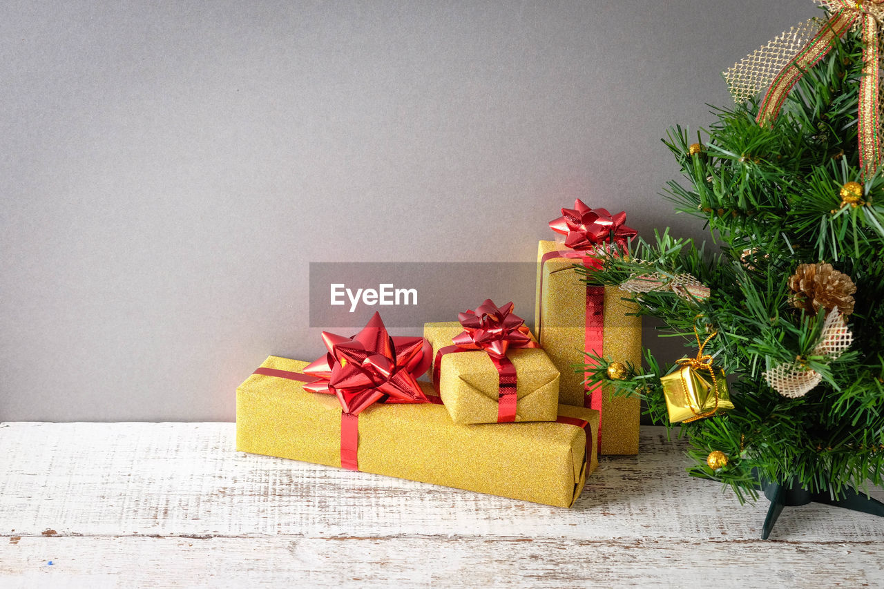 Close-up of christmas tree and presents against gray wall