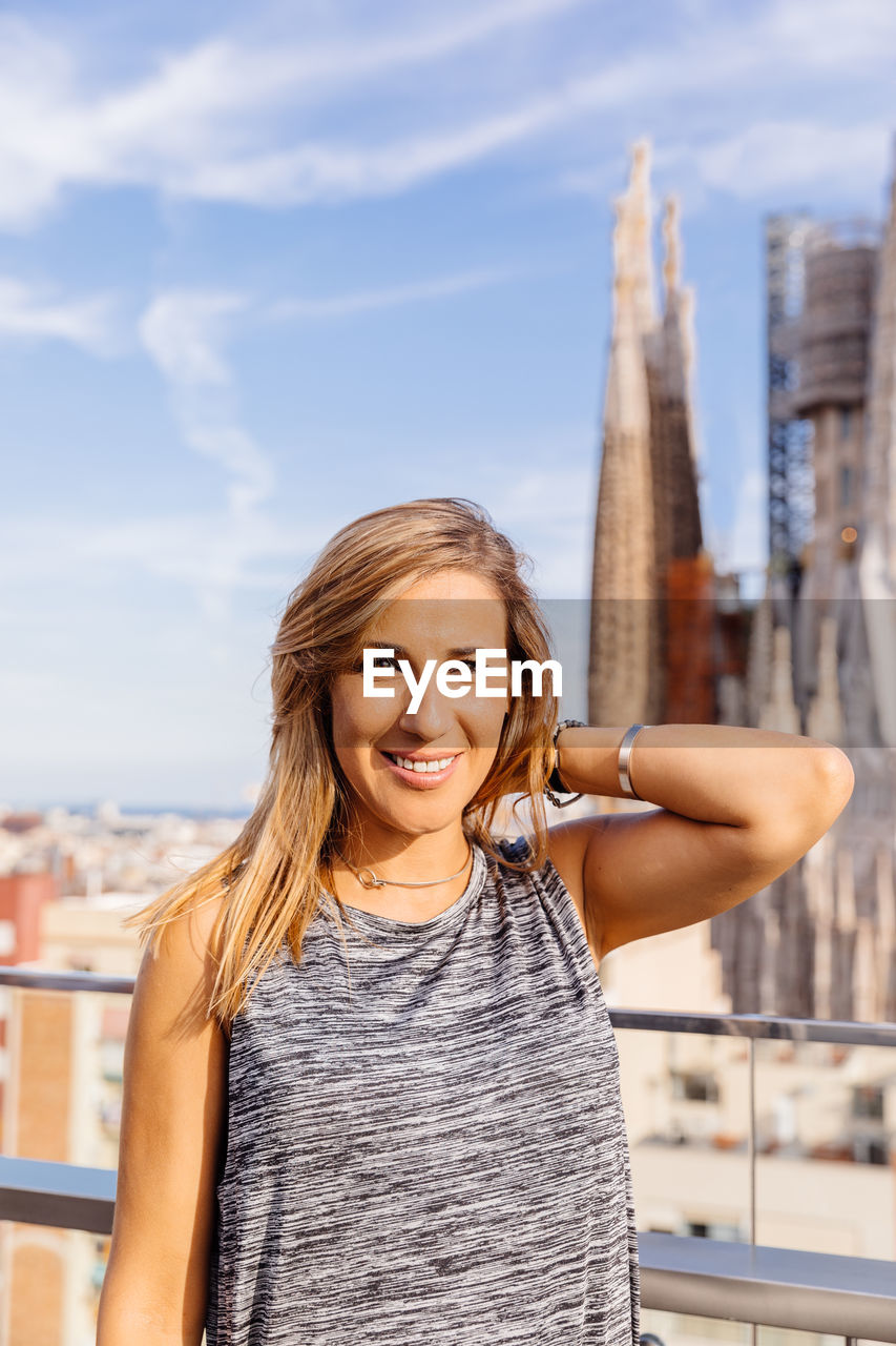 Portrait of smiling young woman standing with buildings in background