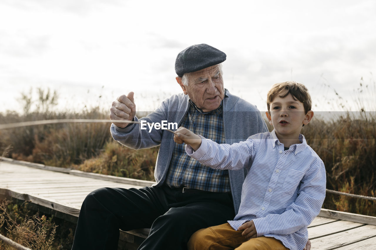 Grandfather and grandson sitting with on boardwalk relaxing