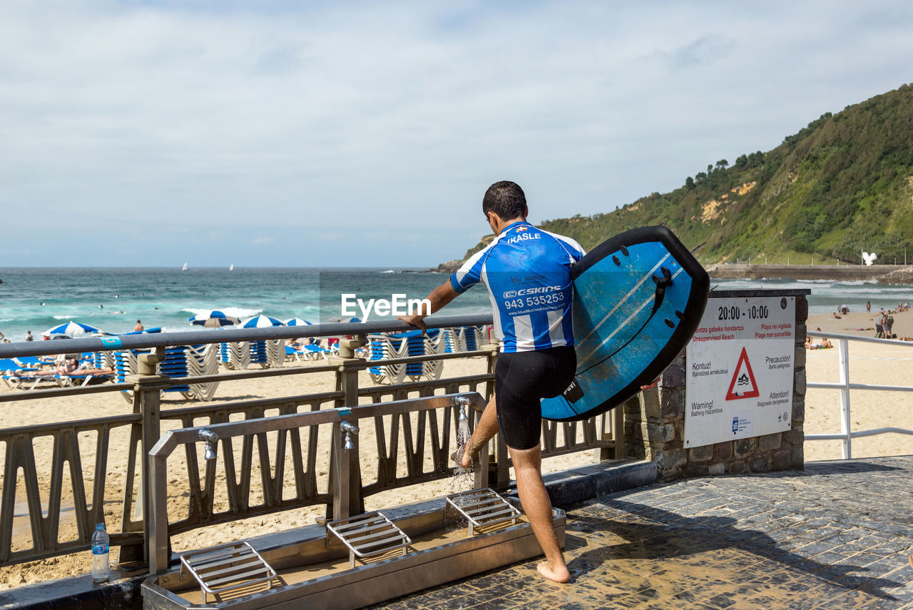 Rear view full length of surfer washing leg at beach