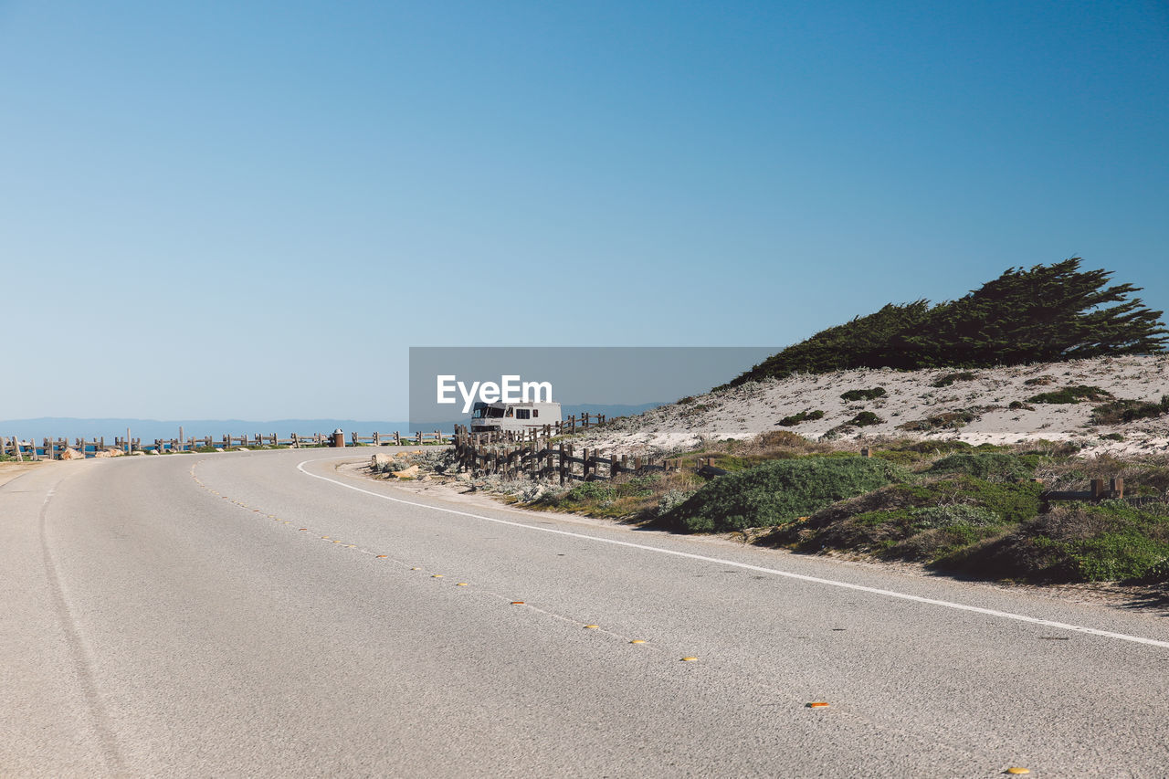 Road by sea against clear blue sky