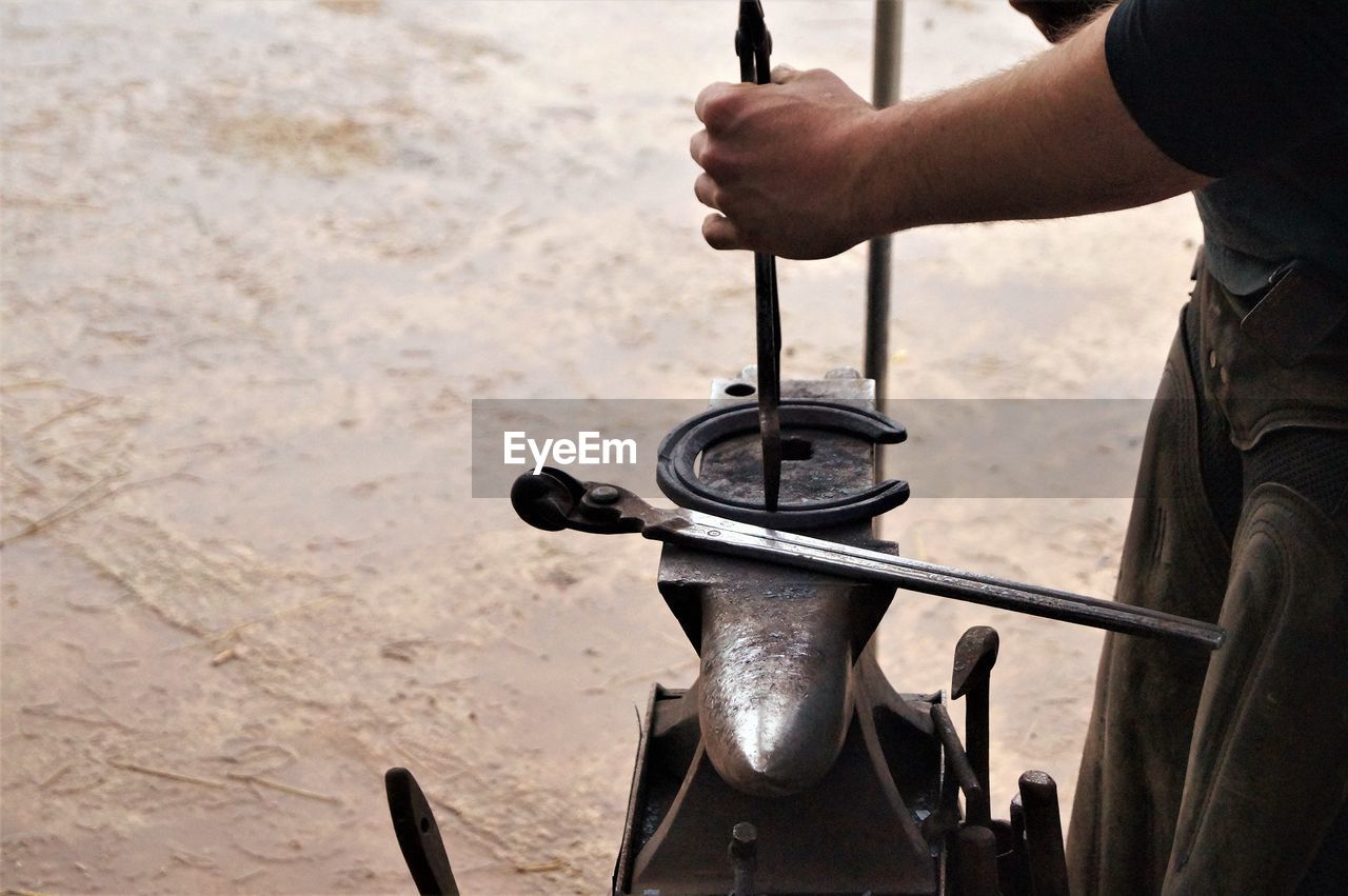 Midsection of blacksmith making horseshoe on anvil