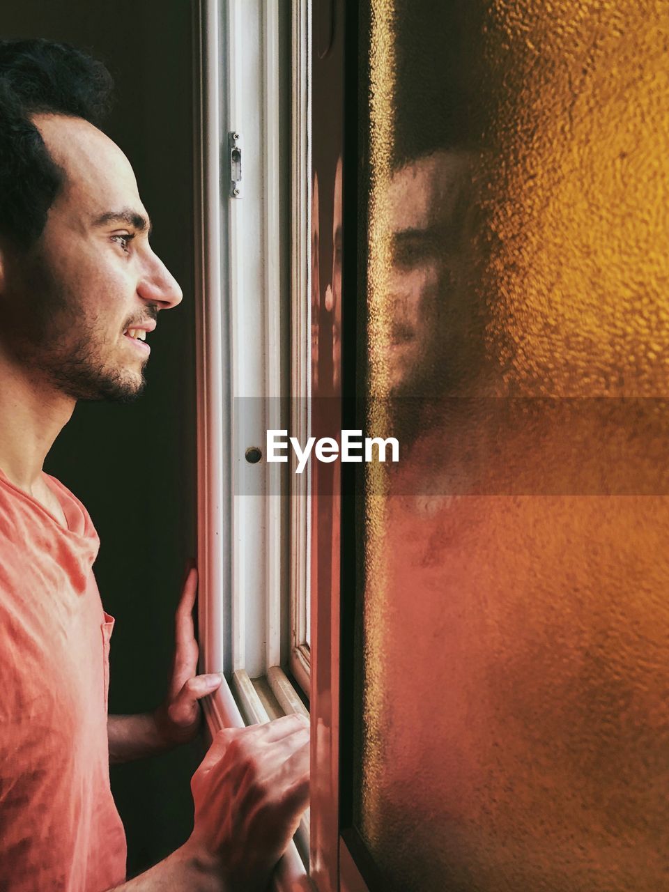 Profile view of man looking through window at home
