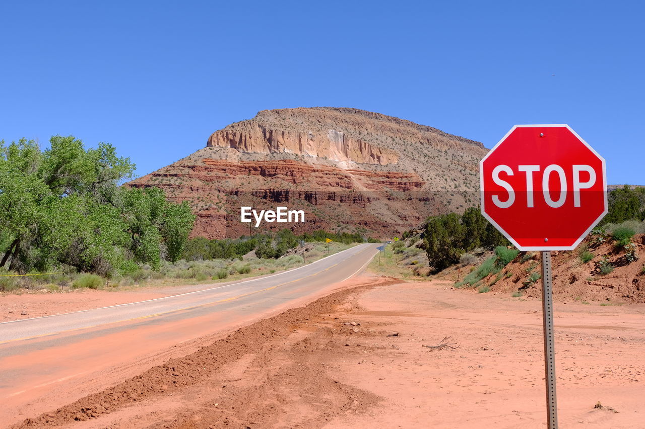 Road sign in desert against clear blue sky