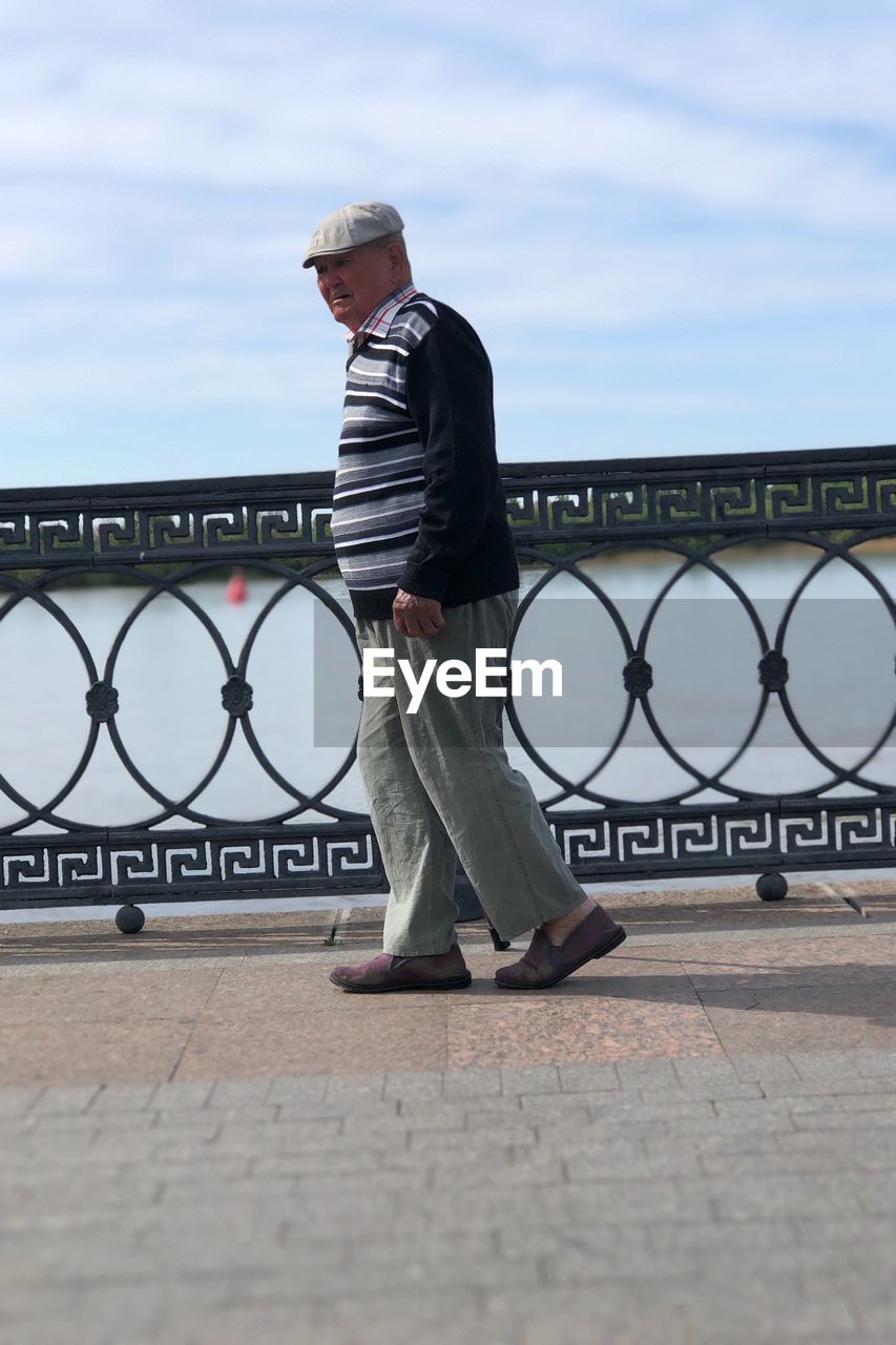 Side view of man standing by railing against sky