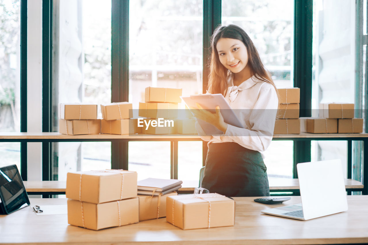 Portrait of smiling young businesswoman standing by packages at office