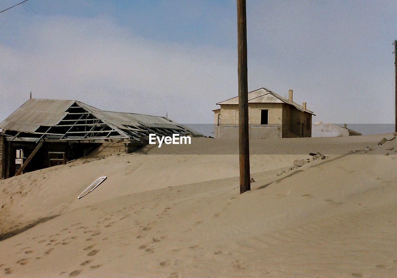 Abandoned houses on sand dunes against sky