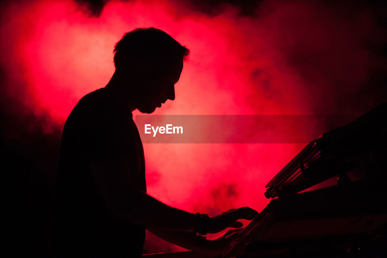 Side view of silhouette man playing piano in music concert