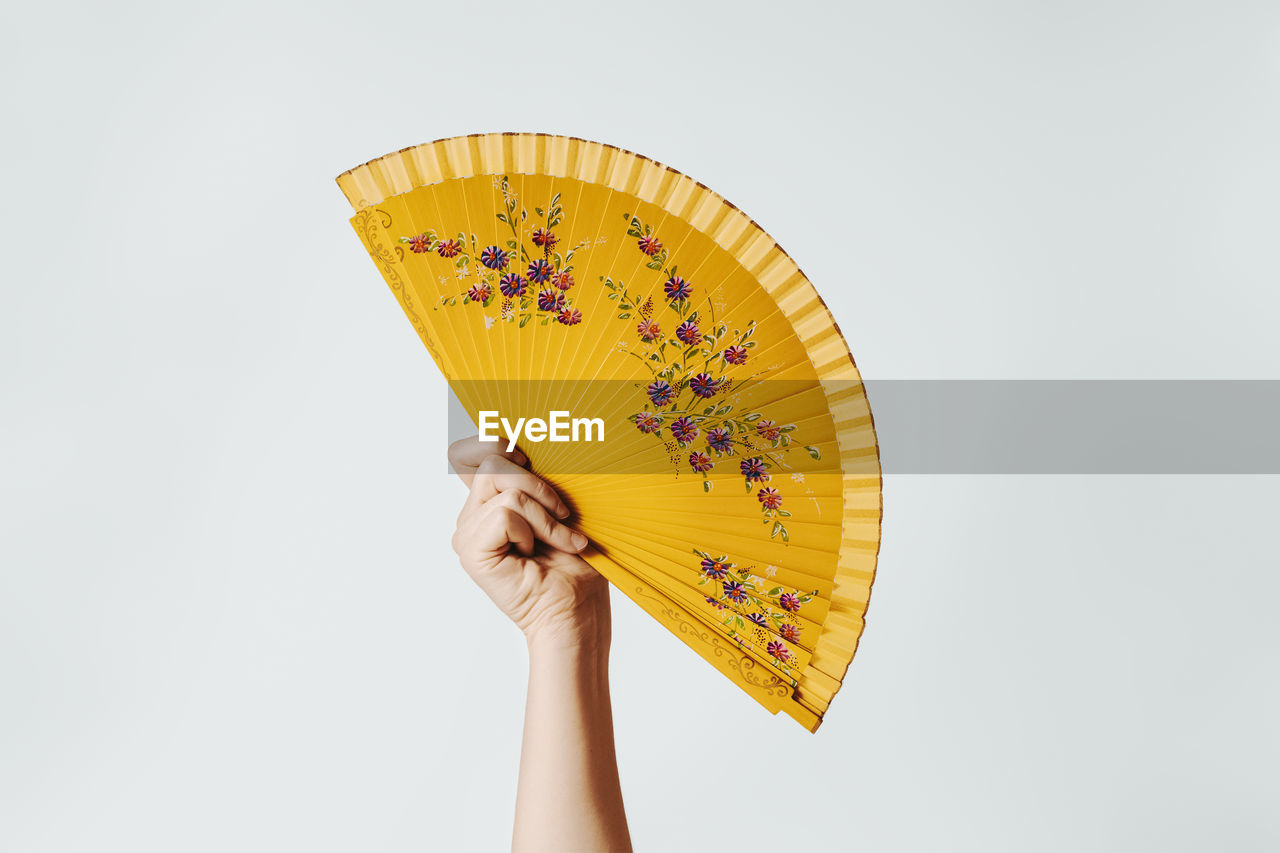 Close-up of woman holding fan against white background