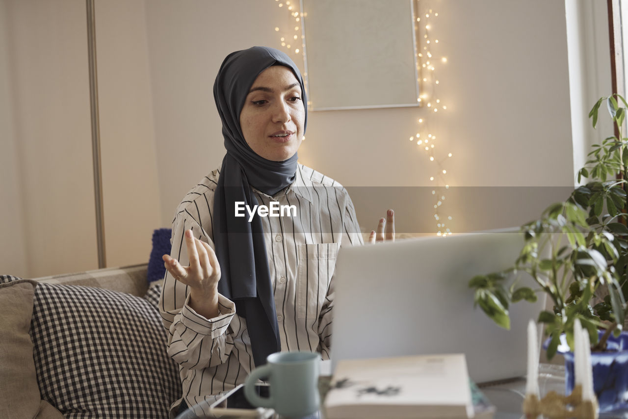 Young businesswoman wearing hijab and discussing on video call over laptop at home