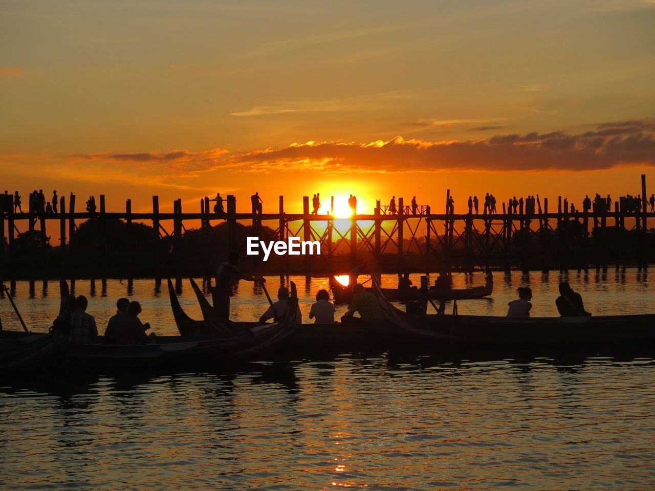 People on boat in river by u bein bridge against sky during sunset