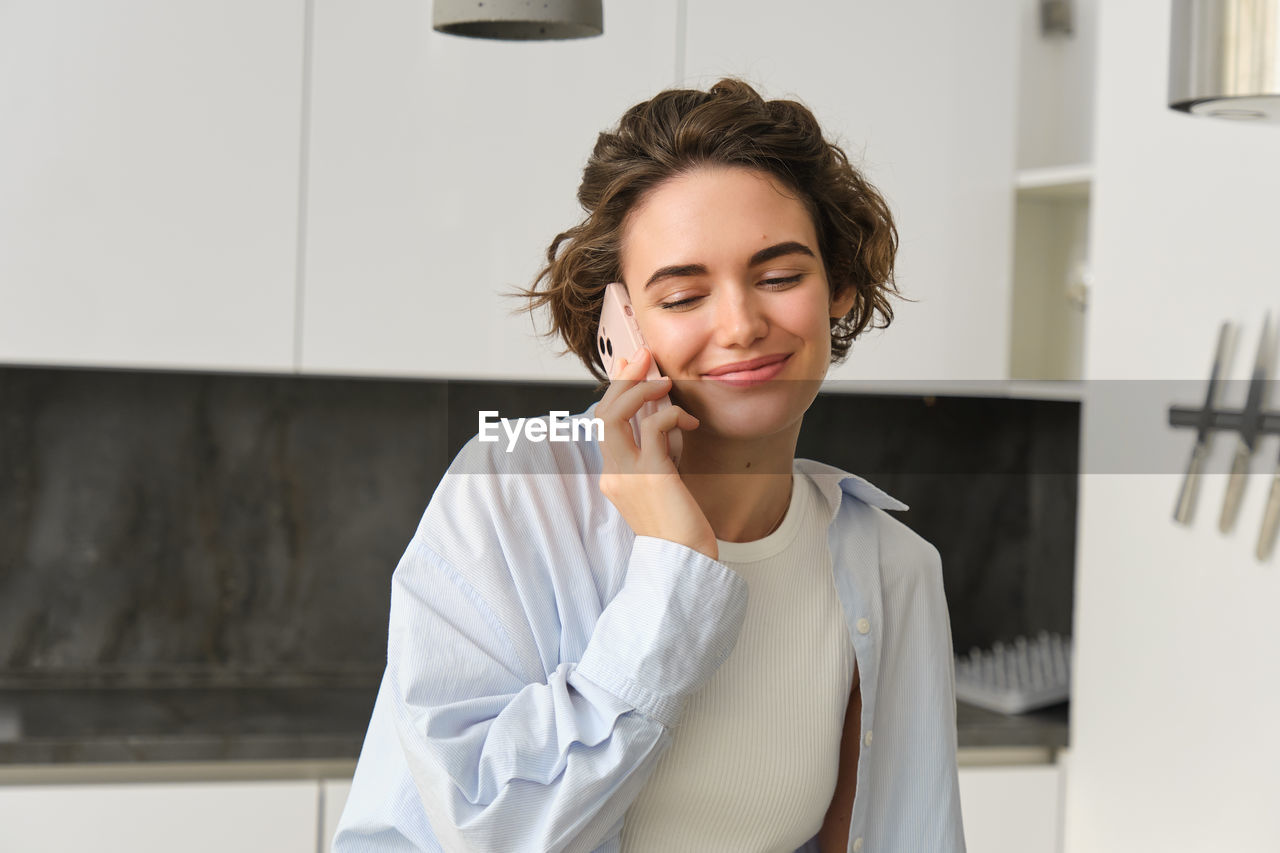 young woman using phone while standing against wall