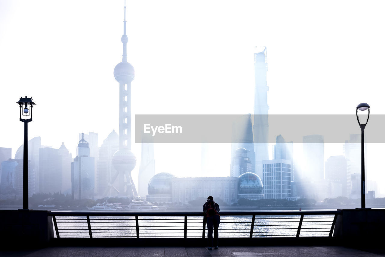 MAN STANDING ON RAILING BY BUILDINGS AGAINST SKY