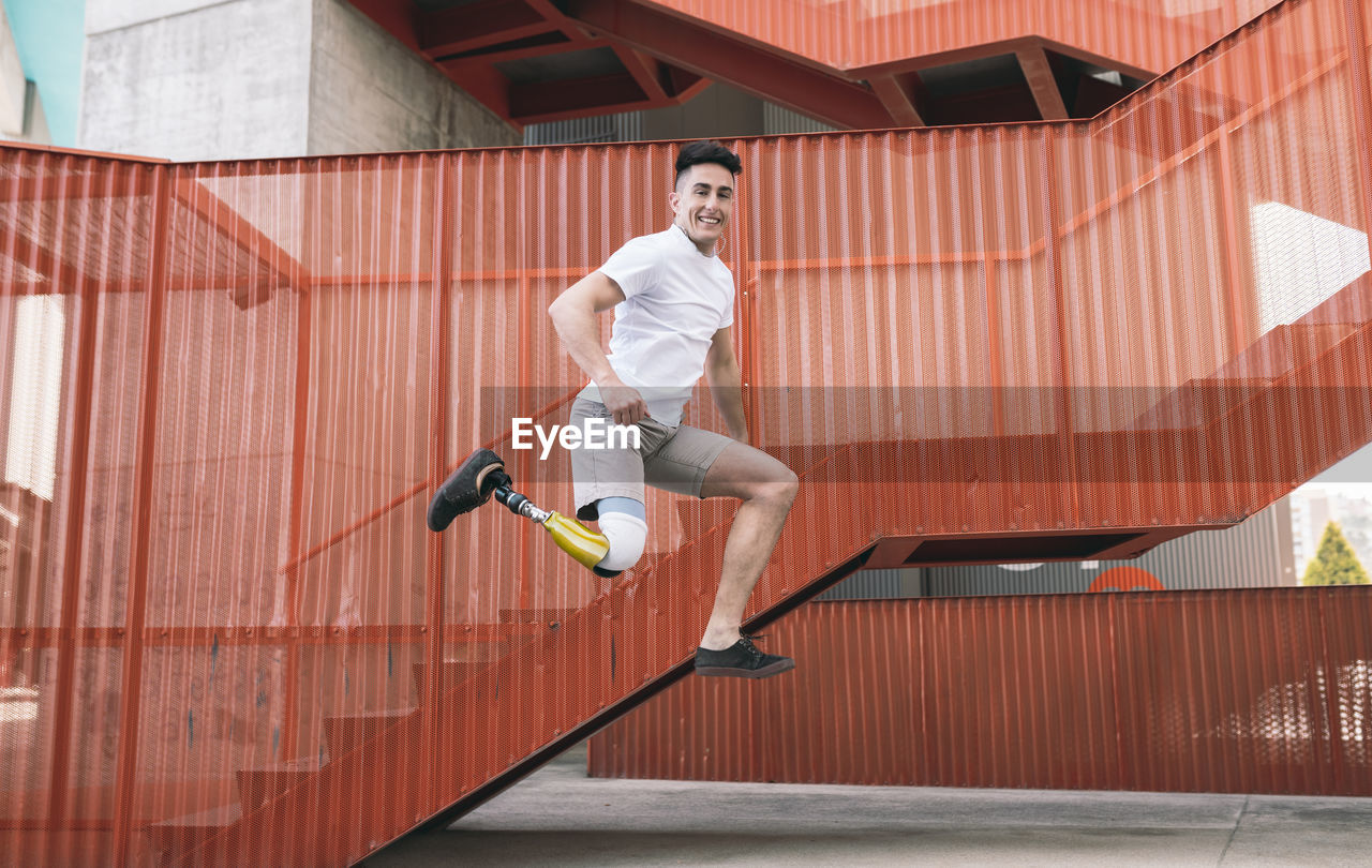 Young disabled man jumping against orange staircase