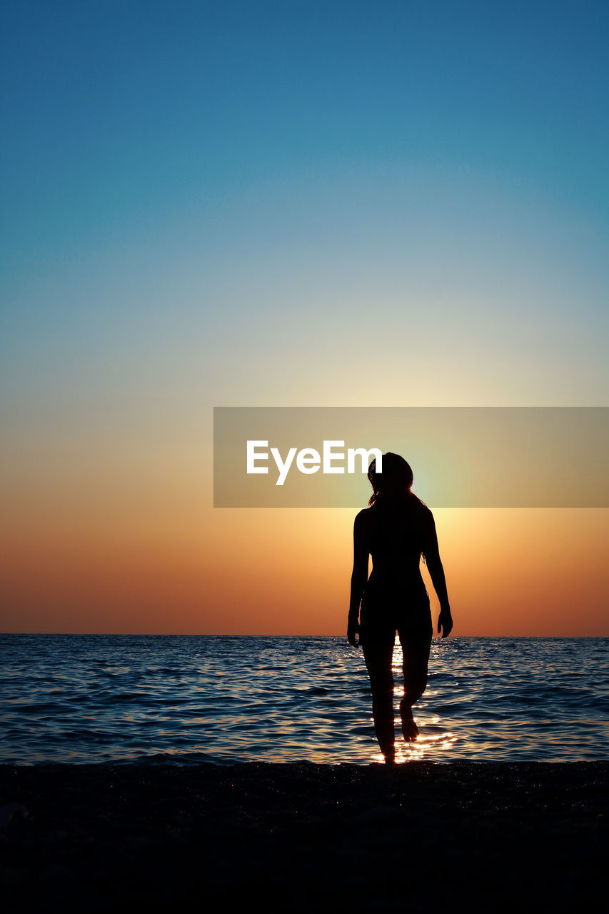 Silhouette woman walking at beach against clear sky during sunset