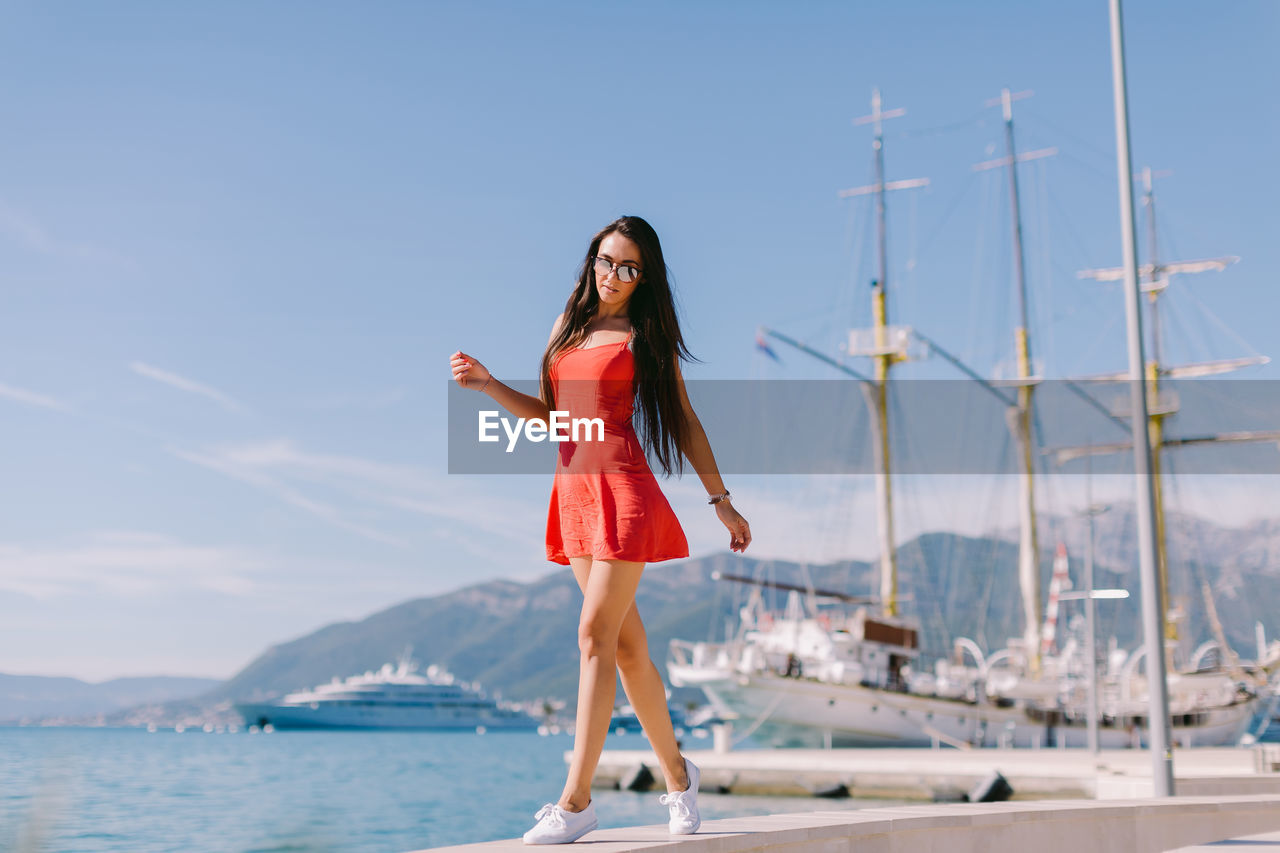 Full length portrait of young woman on promenade by sea against sky